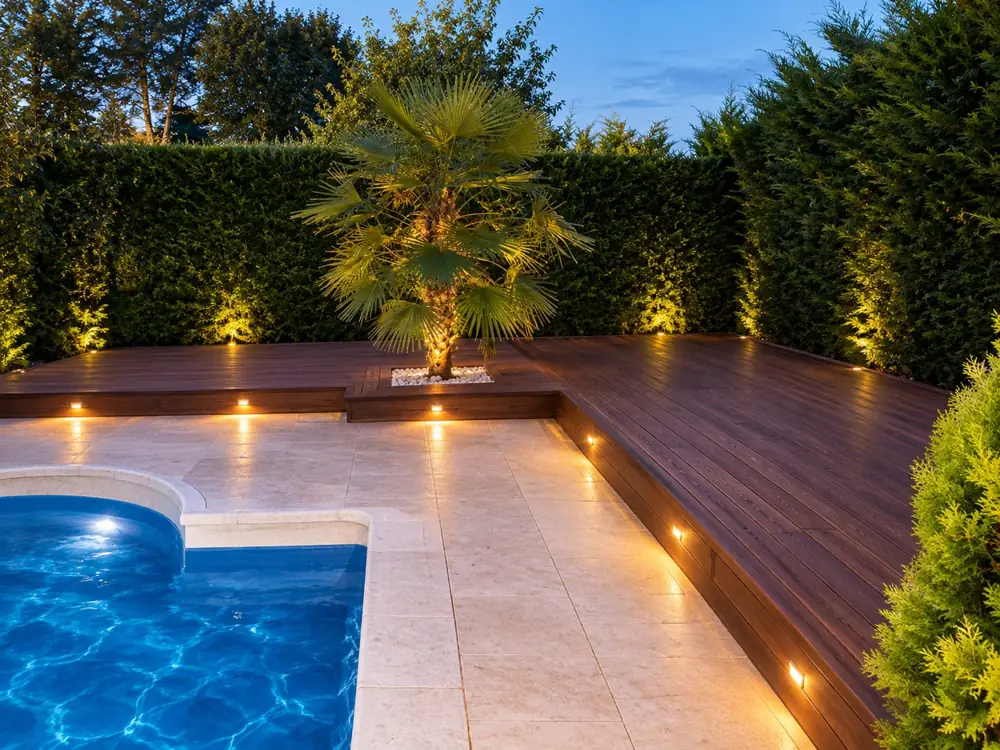 Terrasse en bois illuminée le soir, vue d'ensemble avec piscine