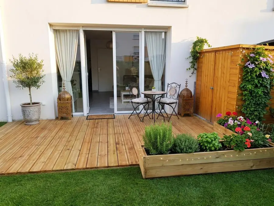 Terrasse en bois devant une baie vitrée avec salon de jardin et bac à plantes
