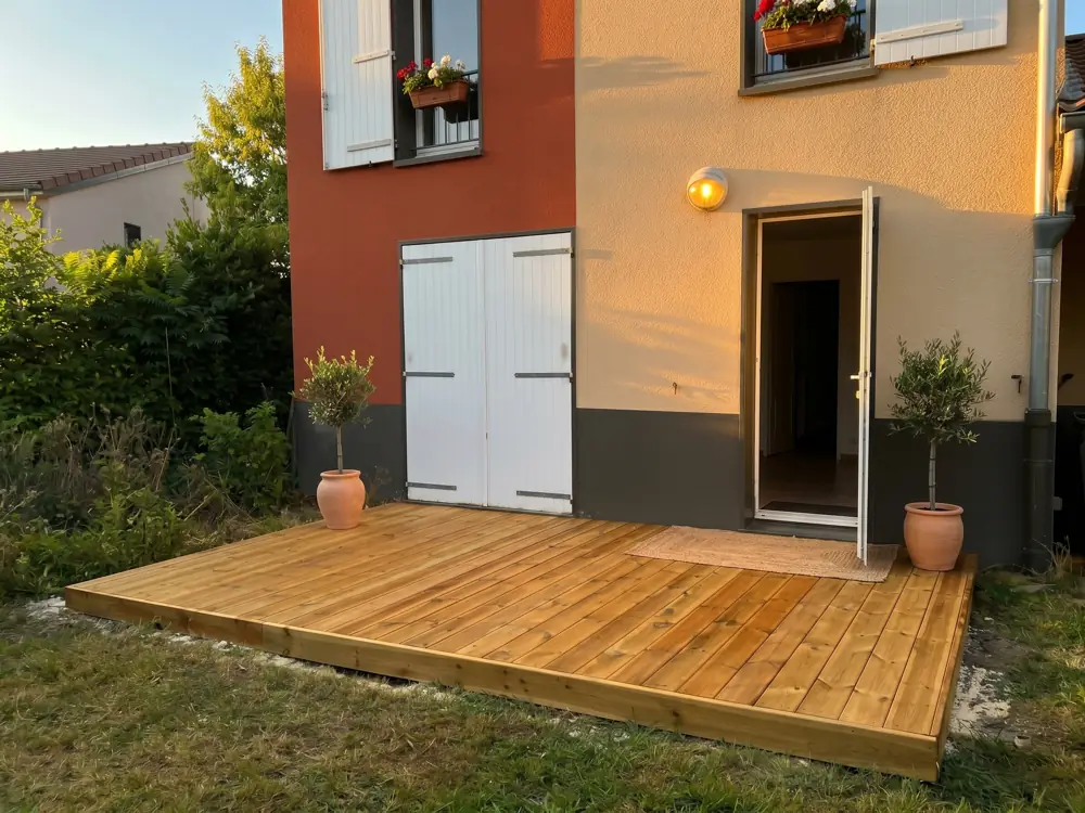 Terrasse en bois devant une maison, avec deux oliviers en pots