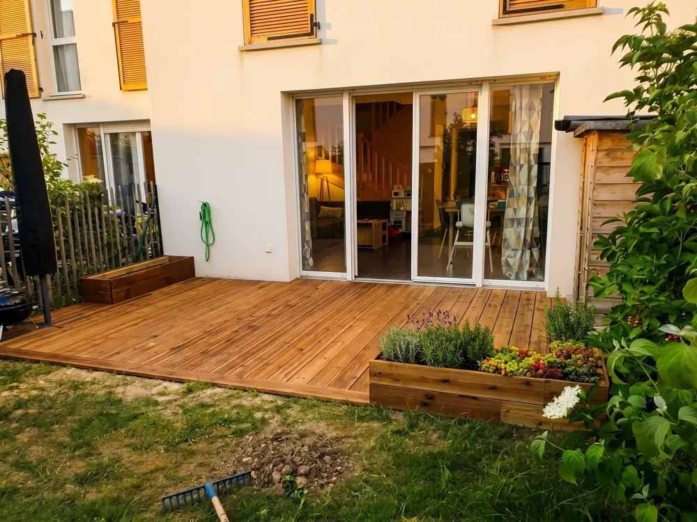 Terrasse en bois avec jardinières, devant des baies vitrées